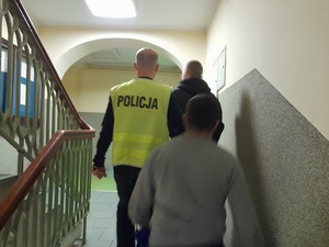 dwaj nieumundurowani policjanci prowadzą schodami zatrzymanego mężczyznę