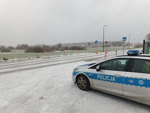 zimowa pora. Śnieg na drodze. Na poboczu stoi policyjny radiowóz