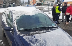 ośnieżony i oblodzony samochód stojący na rondzie. Obok policjant ruchu drogowego rozmawiający z trzema osobami