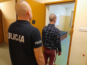 w otwartych drzwiach celi stoi zatrzymany mężczyzna. Za nim znajduje się policjant służby dyżurnej