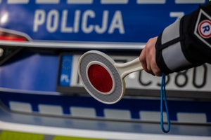 policjant na tle radiowozu trzyma tarczę do kierowania ruchem tzw. &quot;lizak&quot;