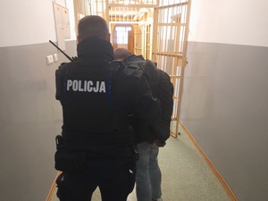 policjant prowadzi mężczyznę skutego kajdankami