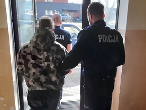 policjant służby konwojowej wyprowadza z budynku komendy zatrzymanego mężczyznę