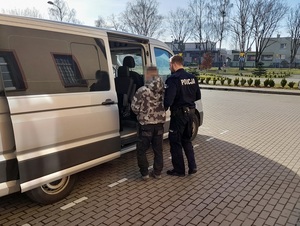 policjant służby konwojowej wprowadza do nieoznakowanego radiowozu zatrzymanego mężczyznę