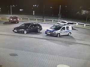 na parkingu stoją zaparkowane obok siebie czarne bmw i policyjny radiowóz