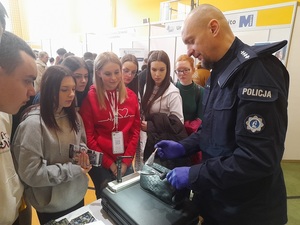 w szkolnej sali sportowej gdzie odbywają się targi edukacyjne, technik kryminalistyki pokazuje zgromadzonej przy policyjnym stoisku młodzieży sposób zabezpieczania linii papilarnych