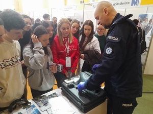 w szkolnej sali sportowej gdzie odbywają się targi edukacyjne, technik kryminalistyki pokazuje zgromadzonej przy policyjnym stoisku młodzieży narzędzia swojej pracy