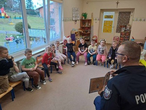 w przedszkolu policjant pokazuje siedzącym przed nim dzieciom książkę