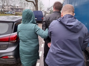 dwoje nieumundurowanych policjantów prowadzi mężczyznę skutego kajdankami w kierunku radiowozu