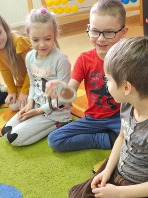 uśmiechnięte dzieci siedzące na dywanie. Chłopiec trzyma kajdanki