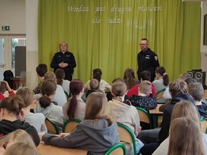 w auli szkolnej dwoje policjantów stoi przed siedzącą na krzesłach młodzieżą