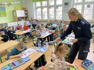 w klasie szkolnej policjantka rozdaje siedzącym w ławkach dzieciom opaski