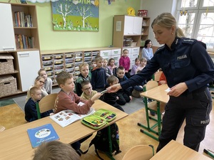 w klasie szkolnej policjantka rozdaje siedzącym w ławkach dzieciom opaski