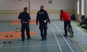 umundurowani policjanci na sali gimnastycznej egzaminują dzieci na rowerach