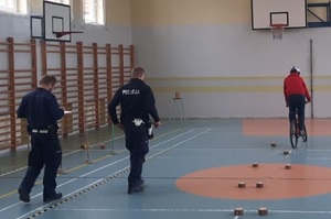 umundurowani policjanci na sali gimnastycznej egzaminują dzieci na rowerach