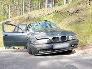 miejsce wypadku drogowego. Na poboczu drogi znajduje się osobowe ciemne bmw z otwartymi drzwiami i rozbitą przednią szybą