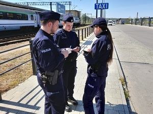 w okolicy dworca PKP na chodniku stoi patrol składający się z trojga policjantów: dwóch policjantów i policjantki. Wszyscy dokonują wpisów do notatników służbowych