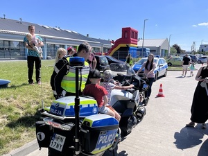 festyn. Na parkingu przed przedszkolem dwoje dzieci siedzi na policyjnym motocyklu. Obok stoi policjant ruchu drogowego