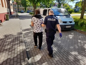 policjant prowadzi zatrzymanego mężczyznę w kierunku nieoznakowanego radiowozu