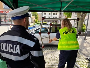 na placu pod namiotem policjantka ćwiczy na urządzeniu do badania refleksu. Obok stoi policjant ruchu drogowego w kurtce motocyklowej