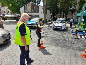 na placu pomiędzy pachołkami idzie kobieta w alkogoglach. Obok idzie policjantka