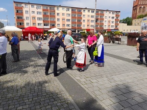 na placu policjantka zakłada dziewczynce w stroju ludowym  opaskę odblaskową na rękę .