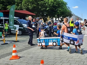 przechadzające się placem dzieci z nałożonymi na siebie autochodzikami. Przed nimi stoi policjantka