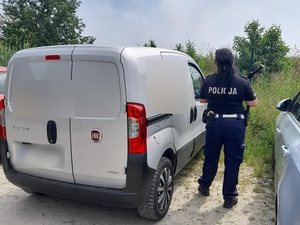 przy przedniej szybie srebrnego fiata fiorino od strony pasażera znajduje się policjantka trzymająca tonfę