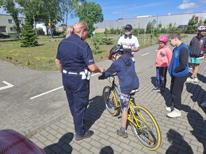 miasteczko ruchu drogowego. Policjantka rozmawia z chłopcem siedzącym na rowerze. Obok stoją uczniowie i ich opiekun