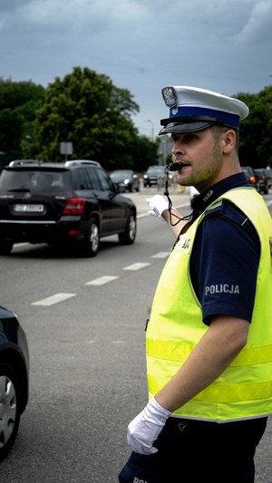 policjant ruchu drogowego z gwizdkiem w ustach kieruje ruchem