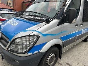 policyjny oznakowany radiowóz mercedes sprinter z poziomą niebieską linią namalowaną farbą w sprayu, ciągnącą się od drzwi kierowcy do przedniej maski