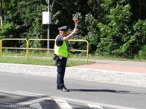 na drodze stoi policjant ruchu drogowego z uniesioną w górę tarczą do zatrzymywania pojazdów