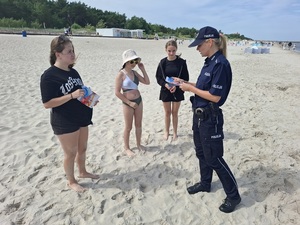 na plaży przy brzegu policjantka wręcza ulotki dziewczynkom