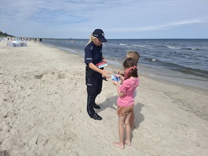 na plaży policjantka wręcza ulotki dwóm dziewczynkom