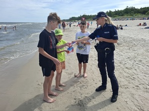 na plaży policjantka wręcza ulotki trzem chłopcom