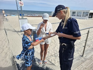 przy wejściu na plażę policjantka wręcza ulotki chłopcu i dziewczynce