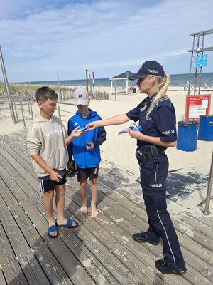 przy wejściu na plażę policjantka wręcza ulotki dwóm chłopcom