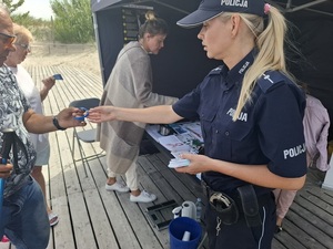 przy stoisku profilaktycznym policjantka wręcza opaskę seniorowi