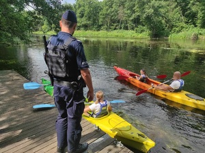 nad rzeką na pomoście stoi policjant, który przygląda się kajakarzom