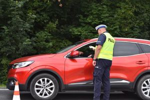 policjant ruchu drogowego mierzy stan trzeźwości kierowcy siedzącego za kierownicą czerwonego SUV-a