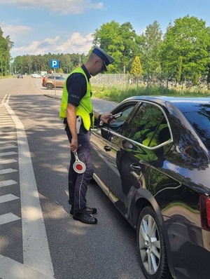 policjant ruchu drogowego sprawdza alkomatem stan trzeźwości osoby siedzącej za kierownicą czarnego samochodu osobowego