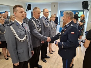 święto Policji obchodzone w auli. Przy ścianie w kilku rzędach stoją mianowani policjanci. Zastępca Komendanta Wojewódzkiego Policji w Gdańsku oraz Komendant Powiatowy Policji w Lęborku wręczają im akty mianowania na wyższe stopnie służbowe