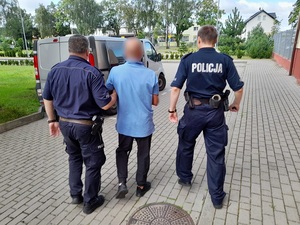 dwaj policjanci służby konwojowej prowadzą zatrzymanego mężczyznę w kierunku nieoznakowanego radiowozu