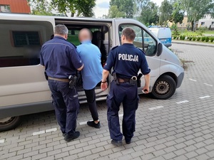 dwaj policjanci służby konwojowej wprowadzają do nieoznakowanego radiowozu zatrzymanego mężczyznę