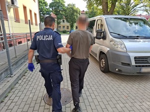 policjant prowadzi zatrzymanego mężczyznę w kierunku nieoznakowanego radiowozu