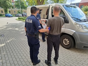 przed nieoznakowanym radiowozem stoją policjant oraz zatrzymany mężczyzna. Drugi policjant otwiera drzwi radiowozu