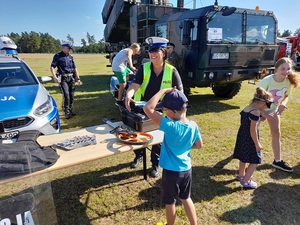 piknik pod chmurką. Przy policyjnym stoisku stoi uśmiechnięta policjantka ruchu drogowego. Przed nią stoi chłopiec