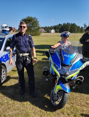 na policyjnym motocyklu siedzi chłopiec. Obok stoi policjant ruchu drogowego