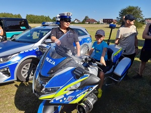 na policyjnym motocyklu siedzi chłopiec. Obok stoi policjantka ruchu drogowego