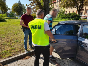 dwaj nieumundurowani policjanci wprowadzają na tylne siedzenie nieoznakowanego radiowozu zatrzymanego mężczyznę